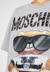 Grå bomullströja med en stor björngrafik som bär solglasögon, texten "MOSCHINO" och en design av läderharnes i nederdelen.