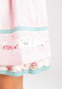 Jupe rose clair en tissu texturé, avec bordure à pois bleus, accents de dentelle et motifs floraux près de l'ourlet.