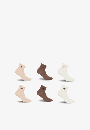 Six chaussettes basses en beige, marron et blanc, chacune arborant un petit logo noir près du bord-côte, présentées sur un fond blanc.