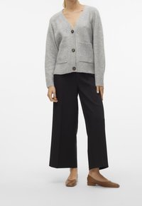 Gray cardigan with a v-neck, button closure, and two front pockets. Paired with black wide-leg trousers and brown flats.