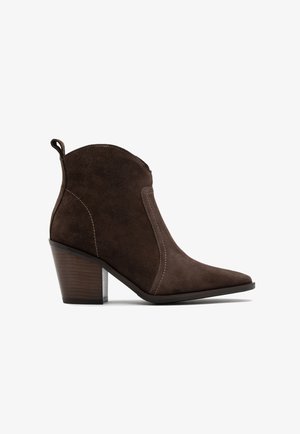 Brązowe zamszowe botki za kostkę z cienkim noskiem i skośnym obcasem. Posiadają kontrastowe szwy oraz uchwyt z tyłu dla łatwiejszego zakupu.