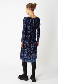 Robe bleu marine à manches longues avec un motif floral bleu, taille cintrée, jupe plissée et encolure ronde, associée à des bottes noires jusqu'aux genoux.