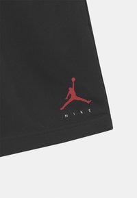 Black athletic shorts with a smooth texture featuring a red Jumpman logo and the word "NIKE" in white, located on the lower left side.
