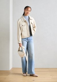 Beige cropped jakke med store frontlommer, sammen med lyseblå vide jeans. Beige håndveske med skulderreim og prikkete beige flate sko.