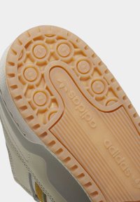 Suela de zapatilla color crema con un diseño de goma texturizada. Presenta patrones circulares y los logotipos en relieve de "adidas" y "sobido".