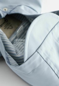 Chemise bleu clair montrant une doublure intérieure avec des rayures blanches horizontales. Présente une texture de tissu lisse et des détails cousus autour du col.