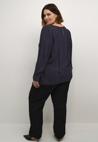 Blusa navy con rayas plateadas verticales, cuello redondo, mangas largas y detalle de ojal en la parte de atrás, combinada con pantalones de pierna ancha negros.
