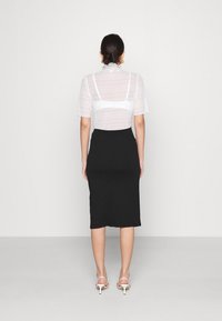 Vit, genomskinlig blus med korta ärmar och volangkrage, kombinerad med en figurnära svart midikjol och vita remsandaler med klack. Bakåtblick.