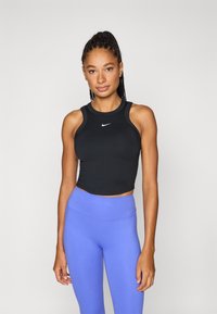 Musta lyhyt urheilutoppi pyöreällä kaula-aukolla ja Nike-logolla, yhdistetty vaaleansinisiin korkeavyötäröisiin leggingsseihin. Sileä kangaspinta.