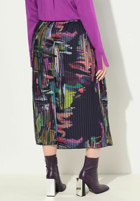 Jupe plissée mi-longue en tissu sombre avec un imprimé abstrait coloré. Associée à des bottines violettes à talons carrés argentés.
