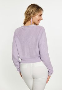 Maglione in lavanda lavorato a maglia con maniche lunghe, orlo a coste e finitura testurizzata, abbinato a pantaloni bianchi a vita alta.