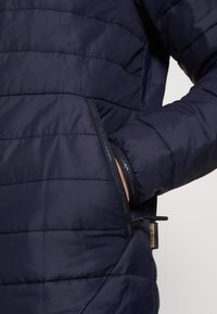 Giacca a vento navy imbottita con motivo trapuntato, dotata di tasca laterale e orlo regolabile. Il materiale è leggero e dalla texture liscia.