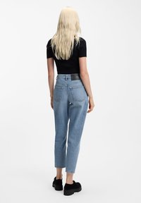 Zili džinsa džinsi ar augstu jostasvietu, taisnu kāju dizainu un aizmugurējām kabatām. Tekstūra ir gluda ar nelielu izbalējušu efektu. Redzama melna jostas lentas etiķete.