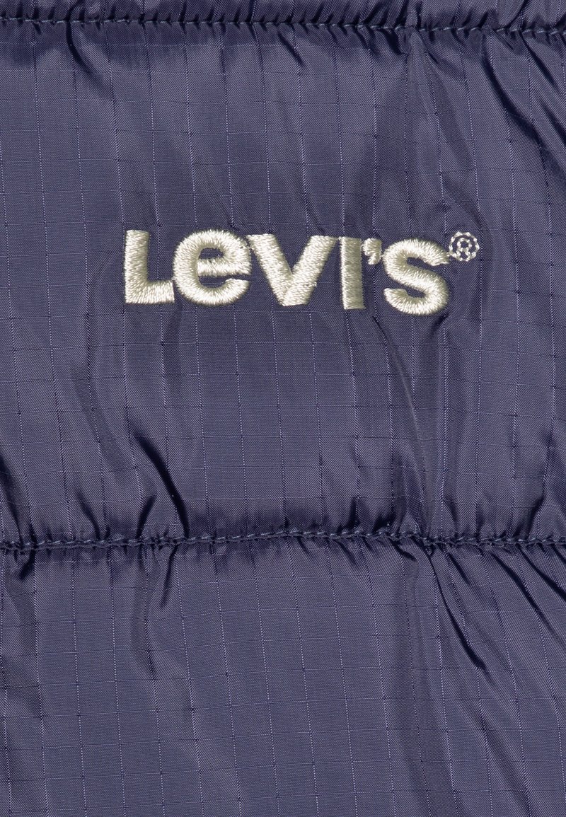 Veste matelassée bleu marine avec des coutures horizontales, une texture brillante et un logo Levi's brodé en gris clair sur le devant.