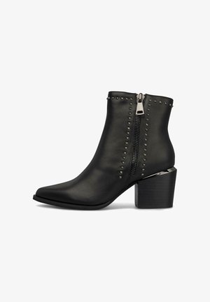 Bottines en simili cuir noir avec des orteils pointus, dotées d'une fermeture éclair latérale et de clous pyramidaux le long de la tige. Talon épais.