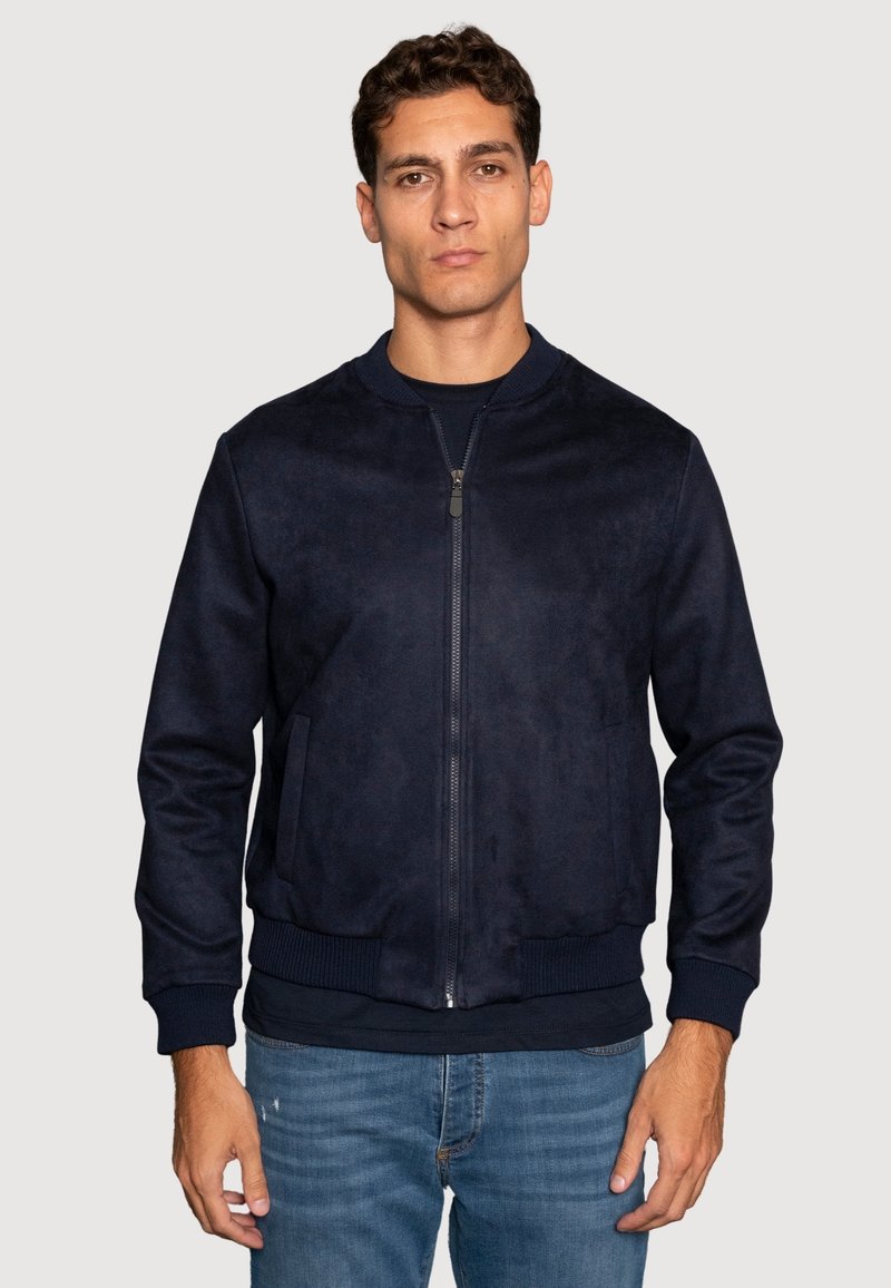 Chaqueta bomber de la marina hecha de suave ante, con cierre de cremallera en el frente, puños y dobladillo acanalados, y dos bolsillos laterales. Llevada sobre una camiseta oscura.