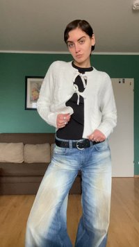 Weißer Strickcardigan mit strukturiertem Muster und Bindebändern, über einem schwarzen Top getragen, kombiniert mit breit geschnittenen, hellblauen Denim-Jeans mit Verblassungen.