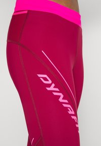 Tight legíny v tmavě burgundské barvě s jasně růžovým pasem. Obsahují jemné švy a diagonální logo ve světle růžové.