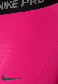 Shorts de sport roses avec une ceinture noire portant l'inscription "Nike Pro" en gris. Le tissu est lisse avec une texture côtelée subtile.