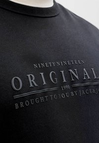 Zwarte crewneck trui met verhoogde tekst waarop staat "Ninety Nineteen Original 1990 Brought to you by Jack & J."