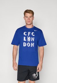 Blå kortærmet t-shirt med "CFC LONDON" i hvid tekst og et lion grafik, lavet af bomuld med rund hals. Nike-logo på ærmet.