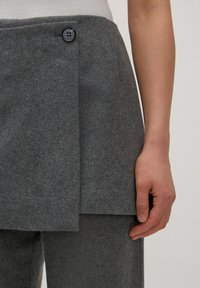 Grijze wollen rok met een gestructureerd ontwerp, voorzien van een enkele zwarte knop en een gelaagde voorkant. Glad materiaal met een getailleerde pasvorm.