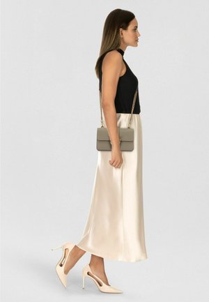 Top nero senza maniche a coste, gonna maxi in raso avorio, décolleté beige con tagli e borsa a tracolla grigia con catena dorata.