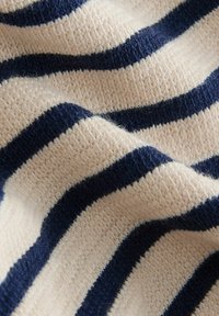 Gros plan sur un tissu tricoté beige avec des rayures horizontales épaisses bleu marine et un motif texturé côtelé.