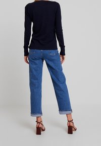 Navy long-sleeve top, light blue loose-fit jeans with rolled cuffs, and brown block-heeled sandals. Simple design with minimal detailing.