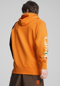 Felpa arancione con cappuccio e pannelli laterali neri, con testo bianco "Carrots" sulla manica sinistra, texture morbida, orlo e polsini a coste.