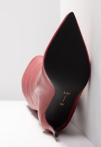 Chaussure à talon haut en cuir rouge avec un embout pointu, présentant une surface texturée, une silhouette épurée et une semelle noire portant des informations de taille et de style.