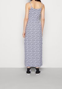 Robe longue avec un fond lavande clair ornée de motifs floraux noirs, bretelles spaghetti réglables et taille cintrée. Portée avec des baskets Converse noires.