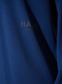 Blauw textuurstof met subtiele "HALO" tekst en cijfers gedrukt in donkere inkt, getoond met licht en schaduw die plooien benadrukken.