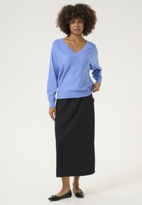 Suéter azul claro de cuello en V con mangas largas, combinado con una falda negra de longitud media y bailarinas negras. Textura de punto suave, ajuste relajado.