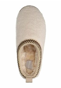 Beige pantoffel gemaakt van pluche materiaal, met een zachte, gestructureerde binnenkant en een decoratieve gestikte rand. Inclusief een lusvormige trekriem aan de achterkant.