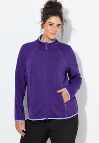 Fioletowa bluza na zamek z wysokim kołnierzem, kontrastowymi jasnoniebieskimi detalami i bocznymi kieszeniami; wykonana z gładkiego, lekkiego materiału.