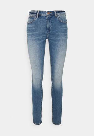 Jeans ajustados de mezclilla azul. Cuentan con un acabado desgastado, diseño clásico de cinco bolsillos y un cierre de cremallera con botón.
