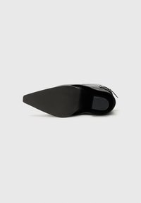 Chaussure à talon noir avec un bout pointu. Dessus en cuir lisse et semelle en caoutchouc texturée. Présente une fermeture éclair sur le côté et de minimalistes accents en métal.