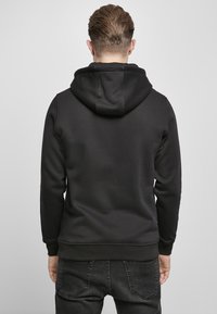 Sudadera con capucha negra hecha de un tejido suave, que presenta un bolsillo tipo canguro y puños acanalados. Diseño liso sin patrones ni acentos visibles.