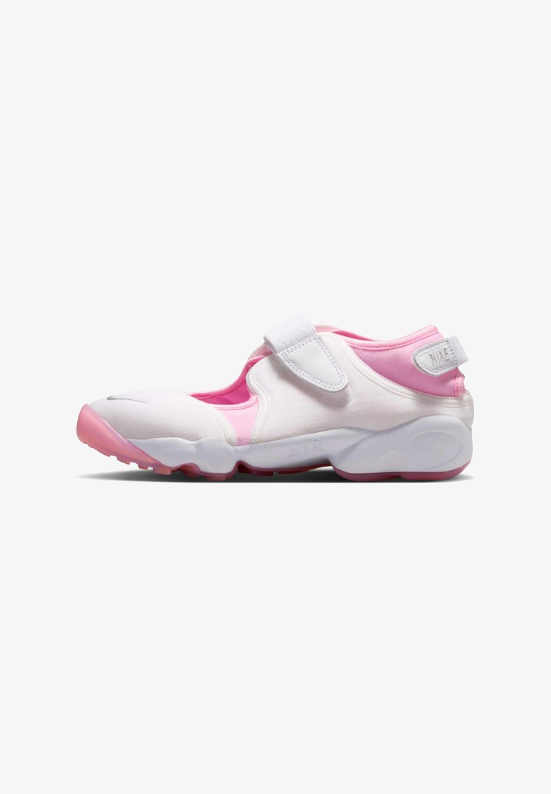 Λευκό και ροζ παπούτσι Nike με ρυθμιζόμενο ιμάντα βέλκρο, μαλακή σόλα και χαμηλό σχεδιασμό, εμφανίζεται από το πλάι σε λευκό φόντο.