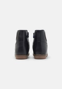 Černé kožené kotníkové boty s hladkým povrchem, kulatou špičkou a hnědou gumovou podrážkou. Obsahují zip a kontrastní detaily šití.