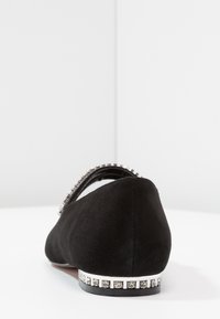 Zapato plano negro de ante con punta redonda y un tacón decorado que presenta una fila de strass a lo largo de la base y una correa en el tobillo.