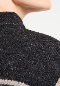 Sweter dziergany z teksturowanej czarnej tkaniny z jasnoszarymi akcentami, zbliżenie na szczegóły ramienia podkreślające miękki materiał i prążkowane krawędzie.