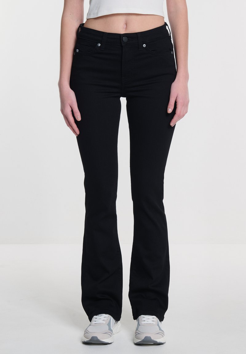 Vaqueros de campana negros de denim, con una cintura ajustada, bolsillos frontales y acentos de metal plateado. La textura es suave y ligeramente elástica.