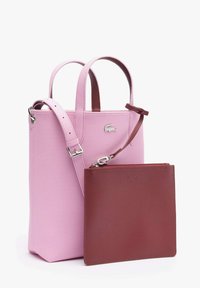 Sac cabas vertical rose avec double poignée et sangle réglable, associé à une pochette bordeaux texturée amovible avec fermeture éclair.