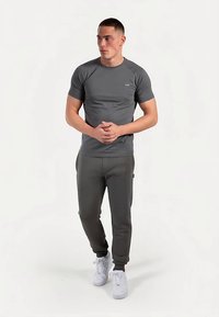 Camiseta deportiva gris de manga corta con logo, combinada con pantalones deportivos a juego y zapatillas blancas, sobre fondo claro.