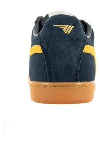 Sneaker in suede blu navy con dettagli a striscia gialla, forma arrotondata e suola in gomma. Accento dorato del logo sul tallone. Texture morbida.