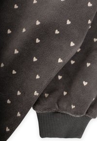 Tissu gris présentant un motif répétitif de petits cœurs blancs. Le matériau semble doux avec un poignet côtelé en bas.