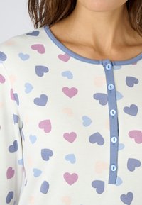 Camiseta de manga larga con una tela suave, presenta un fondo blanco decorado con corazones en tonos pastel de color rosa, púrpura y azul, y botones azules.