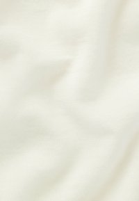 Gros plan sur un tissu doux, blanc cassé, à la surface lisse et légèrement texturée, avec de douces ondulations créant de subtiles ombres.